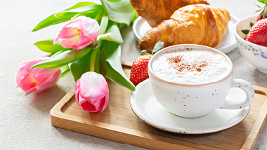 A Cup of Coffee with flowers, fruit, and croissants