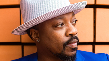 A close up photo of Anthony Hamilton posing in front of a wall.