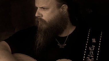 Sepia-toned headshot of country musician Jamey Johnson holding his guitar.