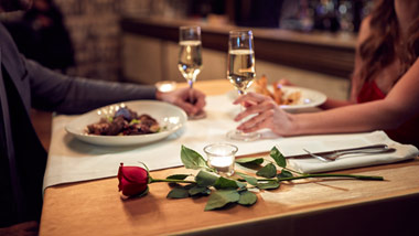 man and woman enjoying a romantic dinner with roses, candles and wine